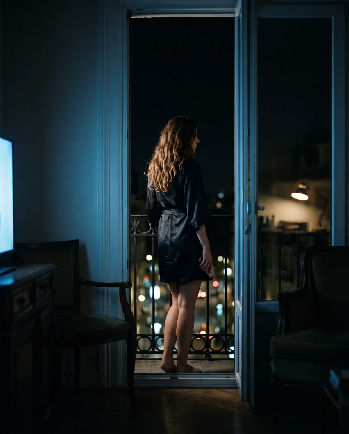 A woman in a silk robe on a balcony over the city at night